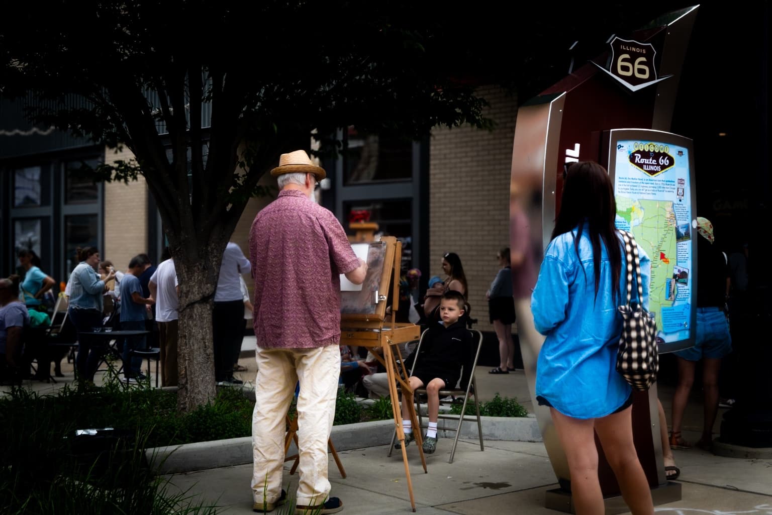 Brian K. Simpson stands at his easel drawing a seated child near an Illinois Route 66 display in Downtown Bloomington.