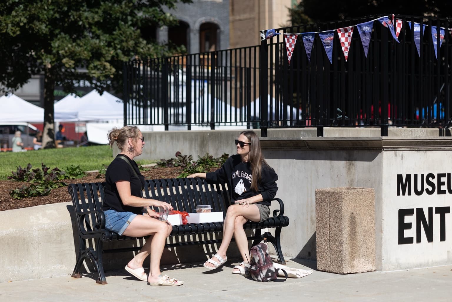 Two people sit facing each other in conversation on a bench outside the McLean County Museum of History.